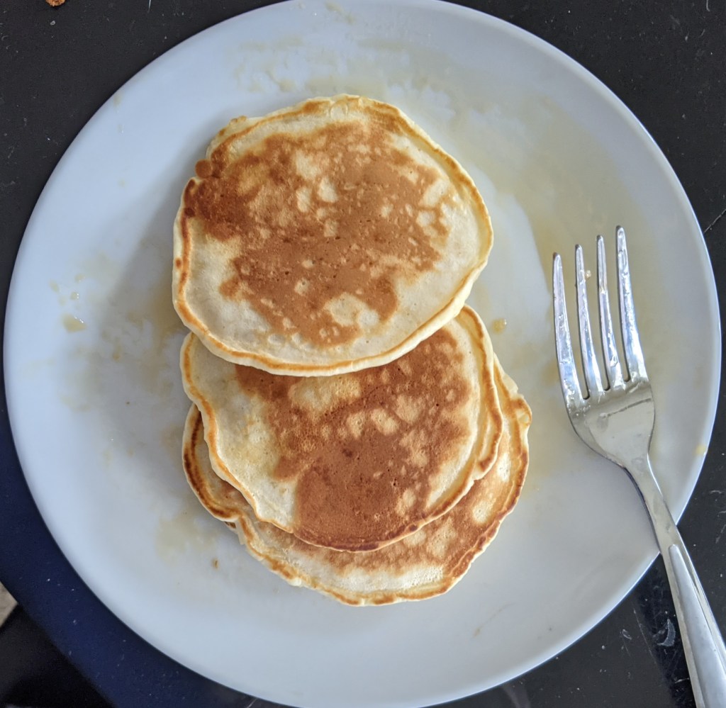 Three pancakes on a white plate with a fork 